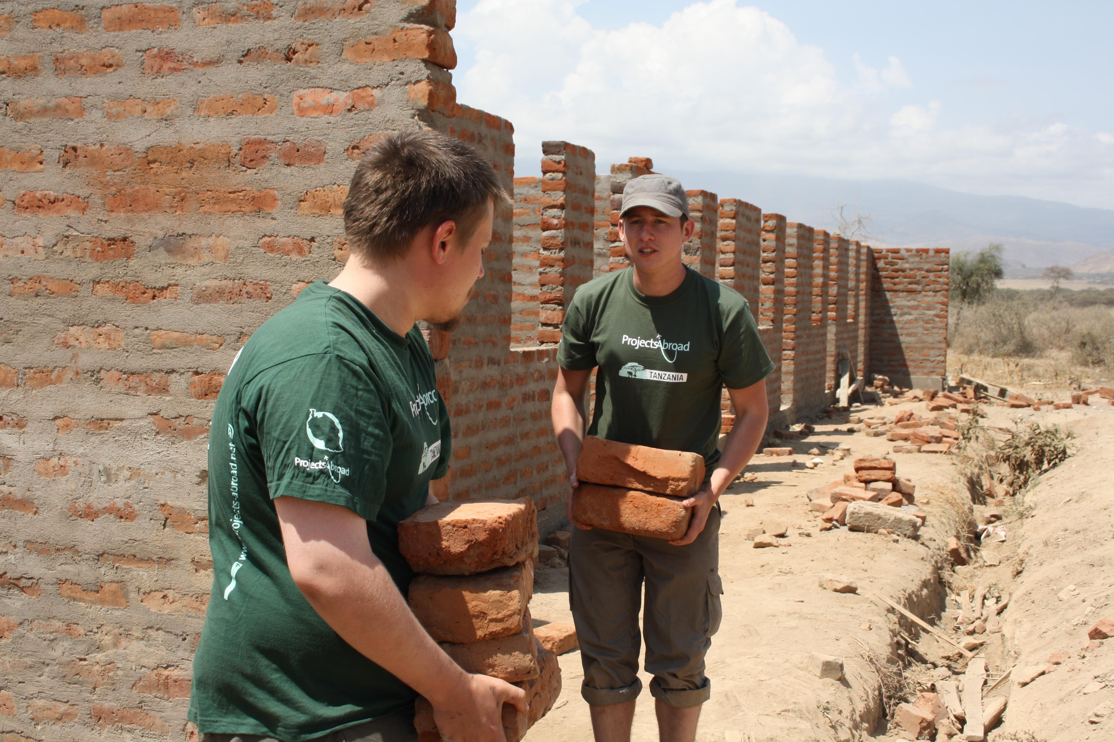 Two male volunteers from Projects Abroad carrying bricks during their building volunteer work in Tanzania Two volunteers are seen carying bricks whilst on their building volunteer work in Tanzania with Projects Abroad